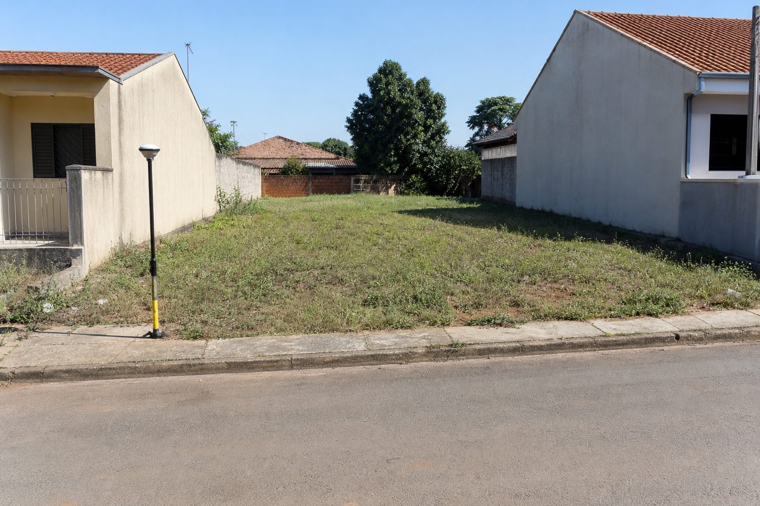 Terreno vazio entre duas casas, numa rua de cidade pequena, com o receptor GNSS num dos cantos do lote